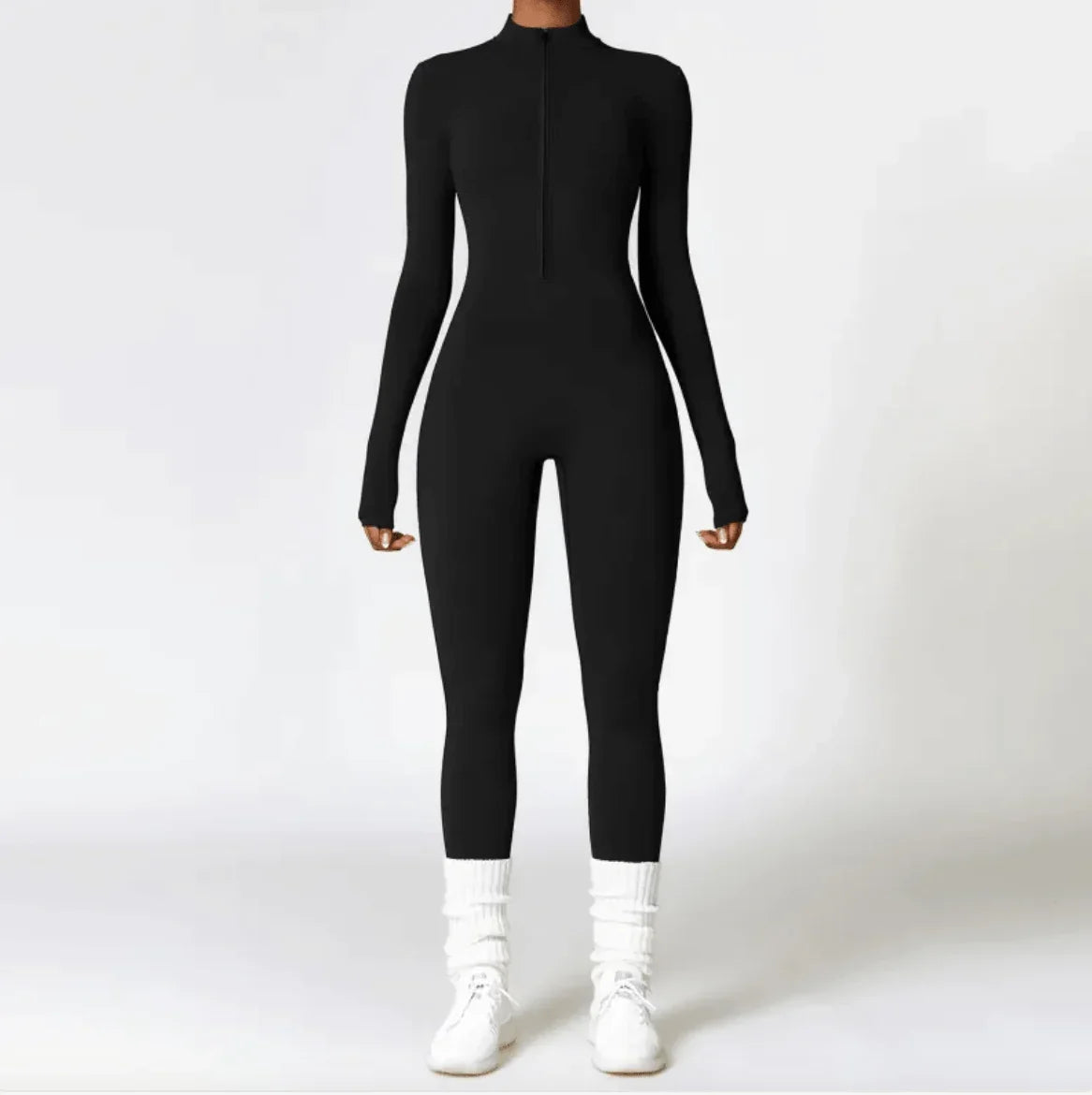 Woman wearing a slim-fit black long-sleeve jumpsuit with white sneakers.