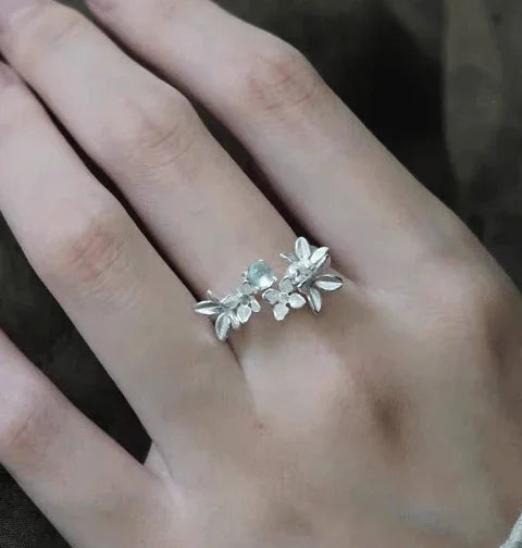 Silver floral ring with delicate flower motifs worn on a finger.
