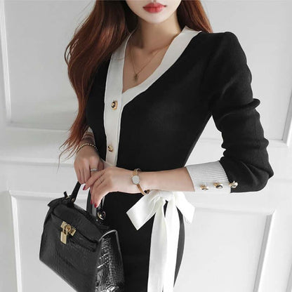 Woman wearing a black and white Lunara knitted dress with long sleeves and a waist bow.